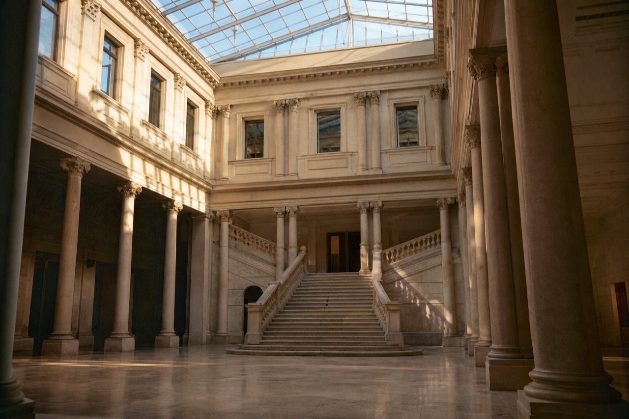 Visitors looking at ancient sculpture in a bright museum gallery with pale stone floors