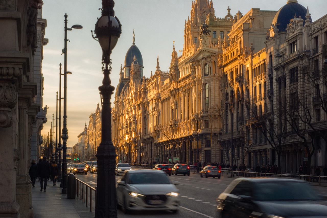Pedestrians crossing a wide boulevard in low evening light between museum buildings