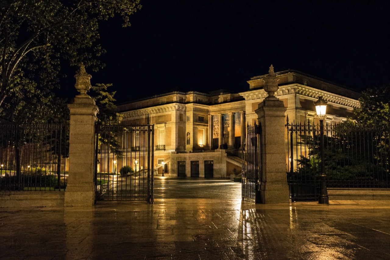 A palace courtyard colonnade with long late shadows across pale stone paving