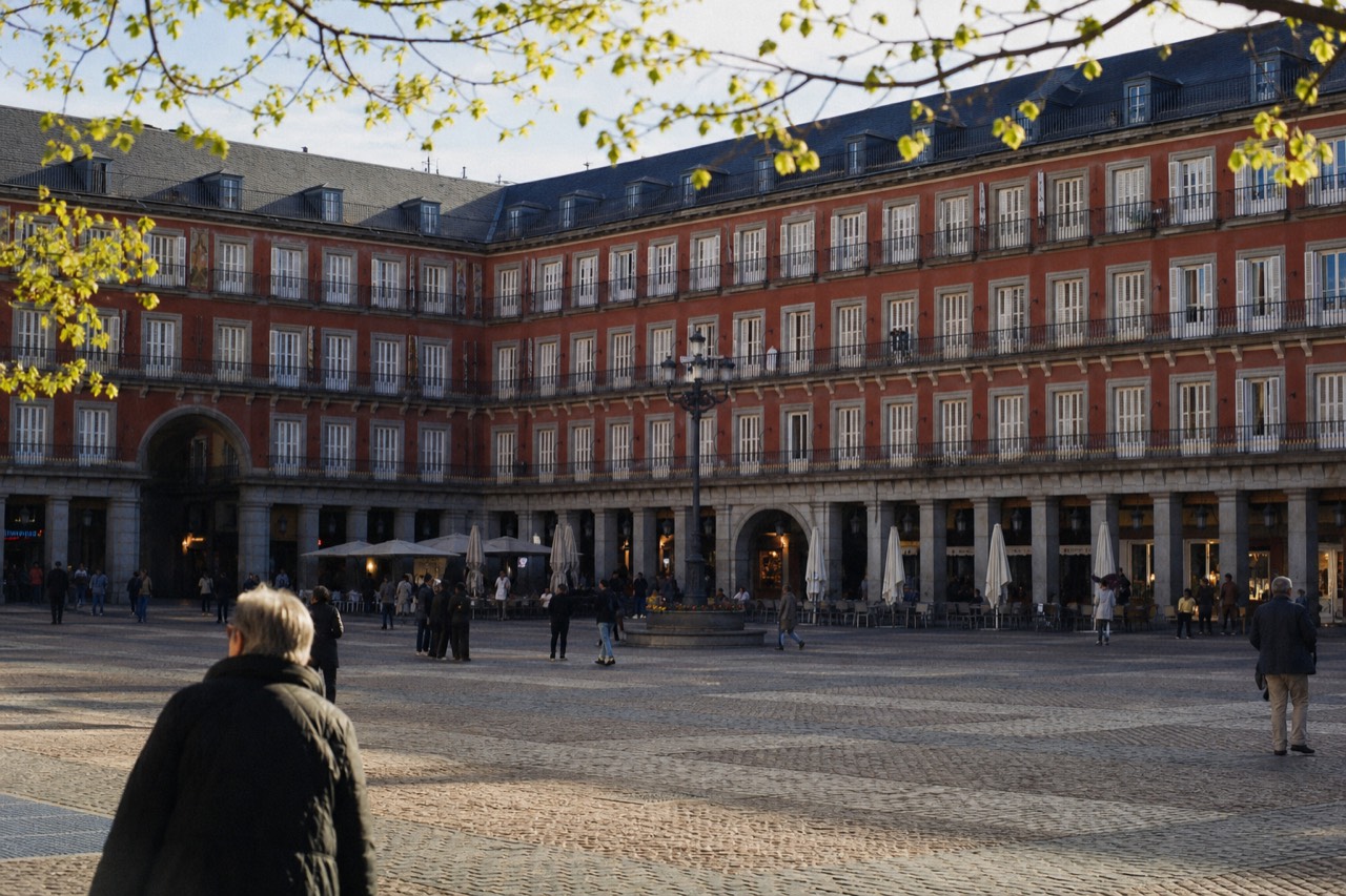 Pedestrians crossing a wide plaza between historic buildings under early evening light