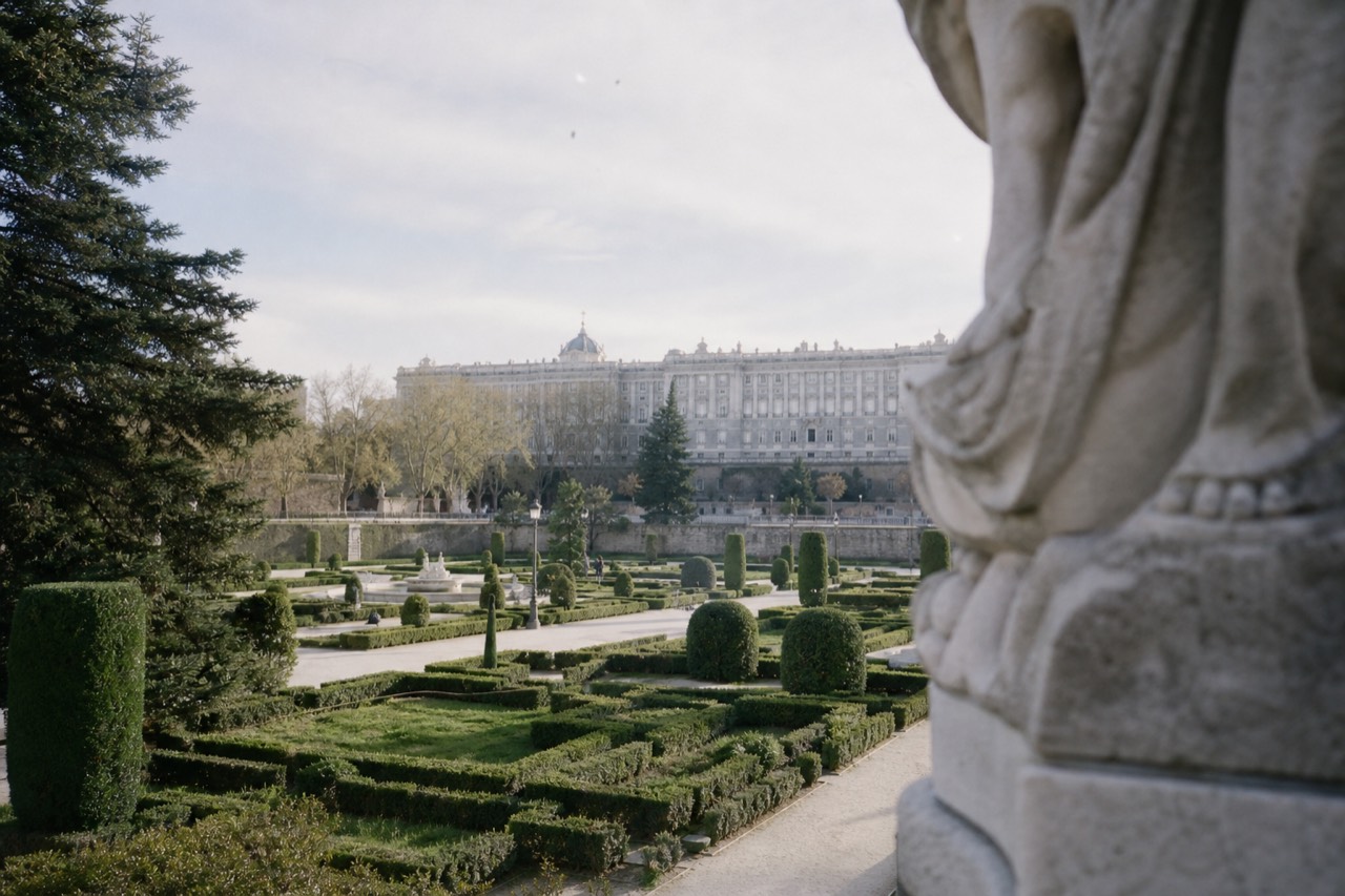 A long pale palace facade seen from a formal garden with clipped hedges