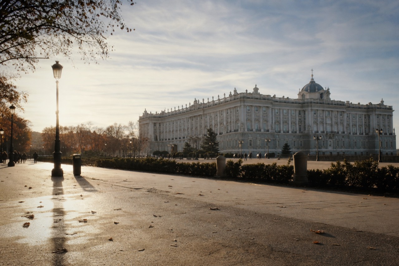 Neoclassical palace facade behind a wrought-iron gate and clipped garden hedges